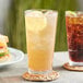 A close up of an Acopa Endure Tritan plastic cooler glass of iced tea with lemon slices and a woven coaster.