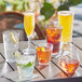 Acopa Endure plastic stackable cooler glasses filled with a variety of drinks on a table.