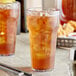 Two Choice clear plastic tumblers of iced tea with ice on a table.