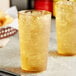 Two Choice Amber plastic tumblers filled with ice and yellow liquid on a table.