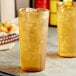 Two Choice amber plastic tumblers filled with ice tea on a table.