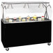 A black and silver Vollrath portable buffet cart with a clear cover over a black counter top with cupcakes displayed.