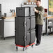 A man using a red dolly to move a stack of black CaterGator pan carriers.