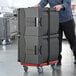 A man pushing a cart with a stack of black CaterGator pan carriers.