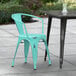 A Lancaster Table & Seating distressed seafoam metal chair on a concrete patio next to a table.
