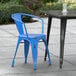 A blue Lancaster Table & Seating outdoor arm chair next to a table on a concrete patio.