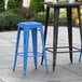 Two Lancaster Table & Seating distressed blue metal barstools on an outdoor patio.