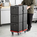 A man pushing a cart with a stack of black CaterGator pan carriers.