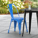 A blue Lancaster Table & Seating outdoor cafe chair sits next to a table.