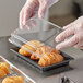 A person in a plastic glove holding a Choice clear plastic container with food, including a croissant.