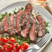 A white plate with grilled Warrington Farm Meats flank steak and tomatoes.