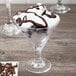 A GET SAN plastic martini glass with ice cream and chocolate drizzle on top.