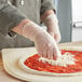 A person wearing Noble Products clear vinyl gloves making a pizza.