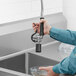 A person using a Regency pre-rinse spray valve on a kitchen sink.