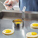 A person using a Choice stainless steel egg ring to fry an egg in a pan.