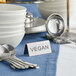 A stainless steel double sided table tent sign that says "Vegan" on a table.