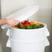 A hand placing a white lid on a Rubbermaid Vegetable Crisper Container full of peppers.