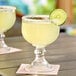 Two Acopa schooner glasses filled with yellow liquid and garnished with a lime slice on an outdoor table.