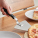 A hand with a black offset handle using a Choice Extra Large Pizza Pie Server to cut a pizza.