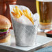A Tablecraft lattice stainless steel fry cup filled with fries served with a burger.