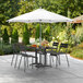 A white Lancaster Table & Seating umbrella over a patio table with chairs.