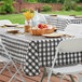 A picnic table with a black and white checkered vinyl table cover and a basket of fruit.