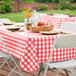 A picnic table with a red and white checkered Choice vinyl tablecloth set with white plates.