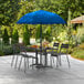 A blue Lancaster Table & Seating umbrella over a table and chairs on an outdoor patio.