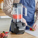A man in a blue apron uses a Hamilton Beach drink blender to make a smoothie with strawberries and blackberries.