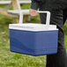A person holding a blue and white Choice cooler with a bail handle.