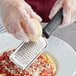 A person in gloves grating cheese on a Choice stainless steel grater with a black handle.
