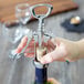 A person opening a bottle of wine with a Choice Wing Corkscrew and Cap Lifter.