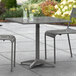 A Lancaster Table & Seating gray metal outdoor table with two chairs on a patio.