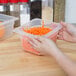 A person holding a Cambro translucent plastic food pan filled with shredded carrots.