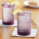 Two Fortessa purple beverage glasses with lemon slices on them.