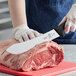 A person using a Mercer American Butcher Knife to cut meat.