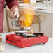 A person cooking food on a red Choice portable gas stove.