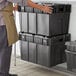 A man holding a stack of black Choice stackable chafer storage boxes.