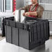 A man in a chef's uniform using a Choice black chafer tote to store a metal container.