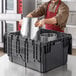 A man in an apron stacking a silver Choice chafer in a black storage crate.
