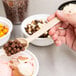 A person holding a Carlisle beige salad bar spoon over a bowl of ice cream with chocolate chips.