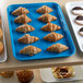 A blue Cambro market tray of pastries and muffins on a bakery display table.