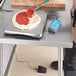 A person measuring pizza dough on a grey AvaWeigh digital scale.