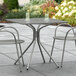 A Lancaster Table & Seating Harbor Gray metal outdoor table with chairs on a patio.