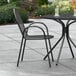 A black Lancaster Table & Seating Harbor outdoor chair and table on a patio.