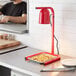 A man using an Avantco red free standing heat lamp to cook food on a counter in a professional kitchen.