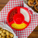A red polypropylene container with tater tots, onion rings, and dipping sauce on a tray.