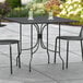 A Lancaster Table & Seating black metal outdoor table with two drinks on it and two chairs.