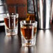 Two Libbey fluted shot glasses filled with brown liquid on a table.