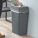 A woman putting a tissue in a Lavex gray rectangular trash can.